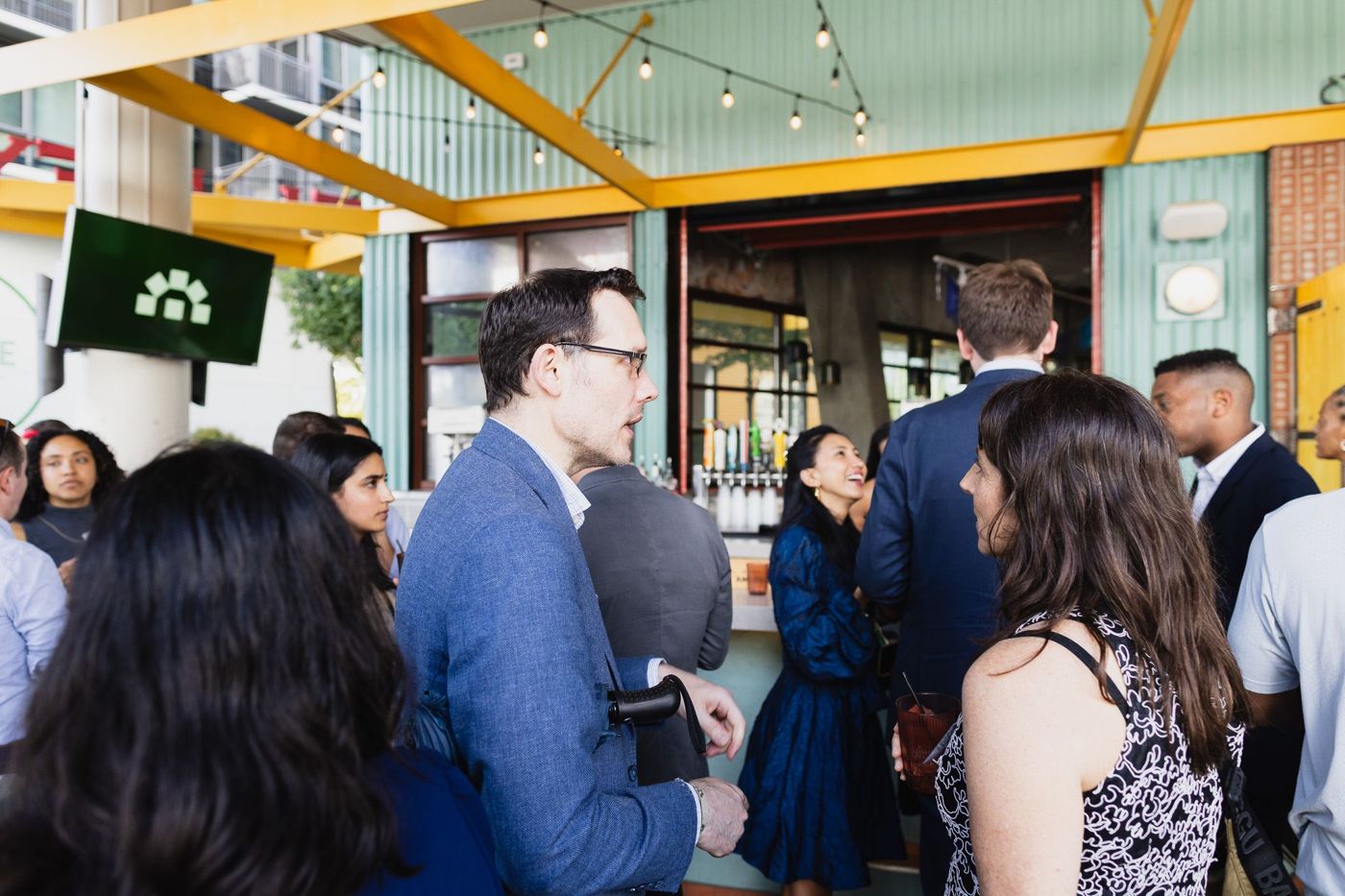 Guests mingling at an outdoor bar under an Orchestra screen