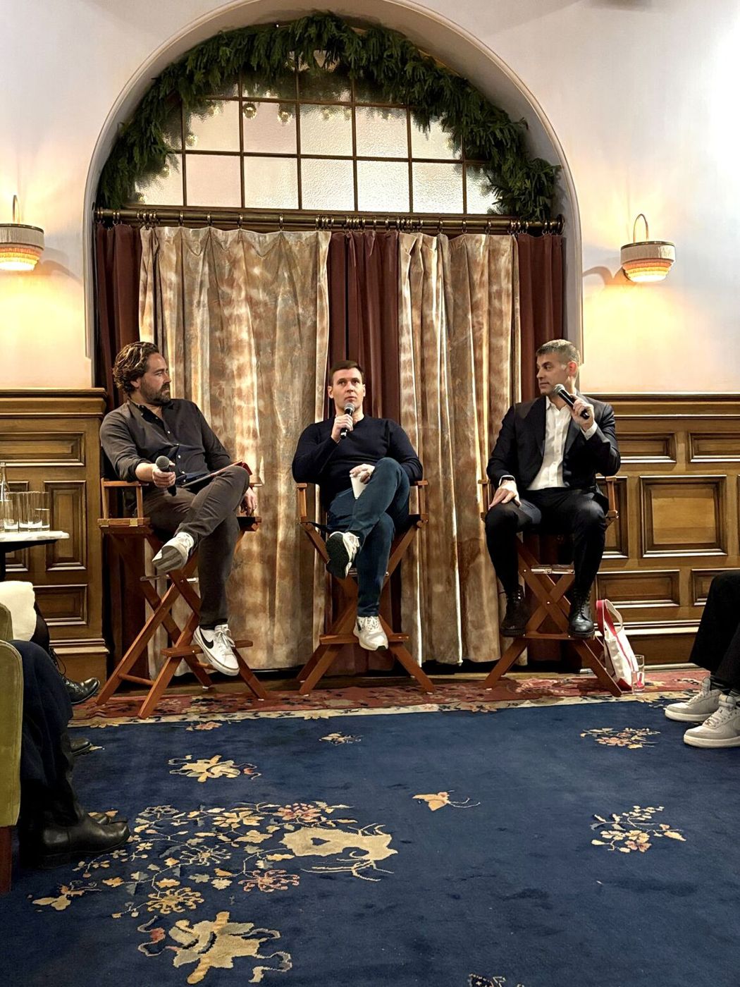Three panelists on director's chairs in a wood-paneled room
